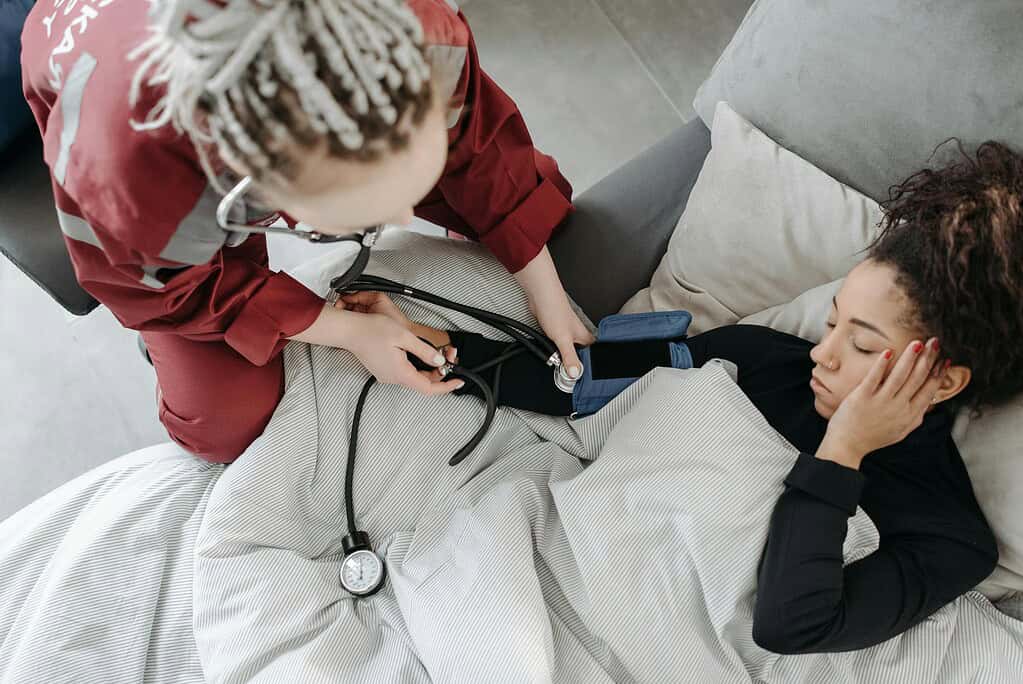 Paramedic measuring patient's blood pressure indoors, illustrating home healthcare assistance.