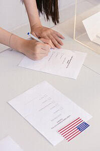 An individual is marking a ballot paper at an election booth, symbolizing democratic participation.