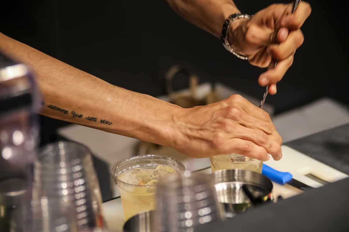 Close-up of a bartender stirring cocktails in an Istanbul bar, showcasing tattoos and craftsmanship.