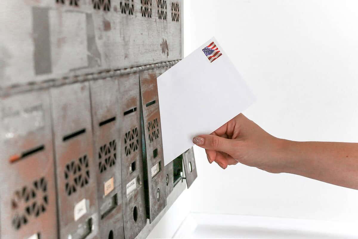 Close-up of a hand inserting a stamped envelope into a mailbox, symbolizing voting.