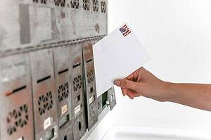 Close-up of a hand inserting a stamped envelope into a mailbox, symbolizing voting.