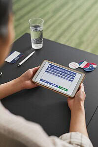 Individual using digital tablet for online voter registration at home.