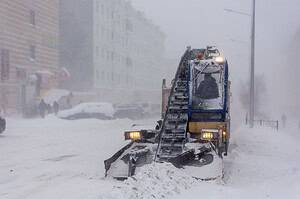 Snow-covered street in city with snow plow clearing heavy snowfall, creating a wintery urban scene.