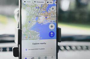 A smartphone displaying GPS map of New York City secured in a car mount during daylight.